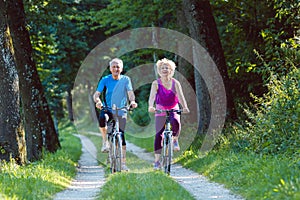 Happy and active senior couple riding bicycles outdoors in the park