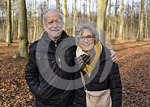 Happy active senior couple walking in sunny autumn forest