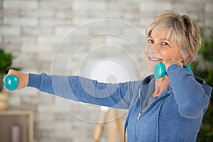 Happy active senior woman doing dumbbell exercises at home