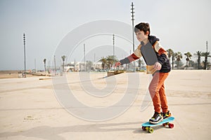 Happy active teenage boy riding on skateboard on an urban skatepark playground, dressed in stylish sportswear.