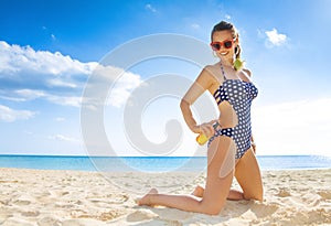 Happy active woman in beachwear on beach applying suntan lotion