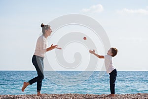 Happy active young family of mother woman and offspring child playing with flying apple on sea beach in spring time