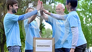 Happy activists putting clothes donation box and giving high five, volunteering