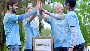 Happy activists putting clothes donation box and giving high five, volunteering photo