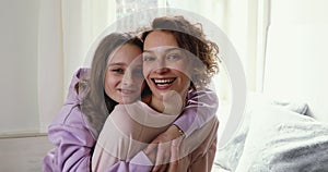 Happy adolescent child girl cuddling back of smiling mother.