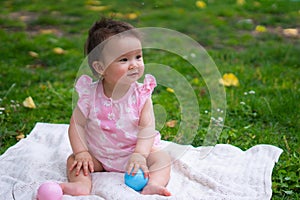 happy and adorable 7 or 8 months old baby girl playing with ball toy cheerful sitting on towel lying on grass city park in