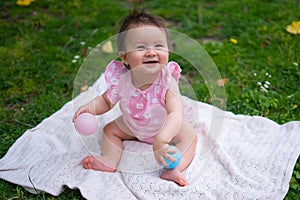 happy and adorable 7 or 8 months old baby girl playing with ball toy cheerful sitting on towel lying on grass city park in