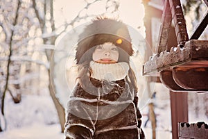 Happy adorable child girl in fur hat and coat near bird feeder on the walk in winter forest