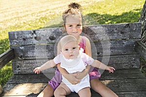 Happy adorable chubby baby girl sitting on a bench with her daughter sister