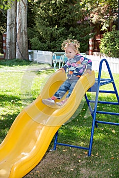 Happy adorable girl on childrens slide on playground near kindergarten Montessori on summer