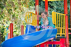 Happy adorable girl with mom on children's slide on playground near kindergarten Montessori