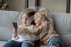 Happy adorable little children playing games on cellphone.