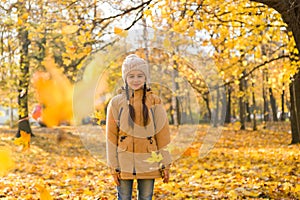 Happy adorable little girl standing in the autumn park enjoying the leaf fall