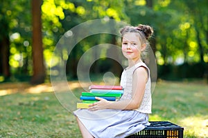 Happy adorable little kid girl reading book and holding different colorful books on first day to school or nursery