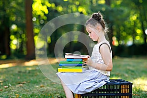 Happy adorable little kid girl reading book and holding different colorful books on first day to school or nursery