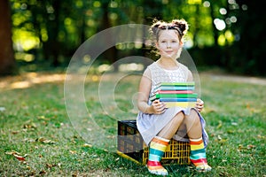 Happy adorable little kid girl reading book and holding different colorful books on first day to school or nursery