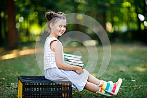 Happy adorable little kid girl reading book and holding different colorful books on first day to school or nursery