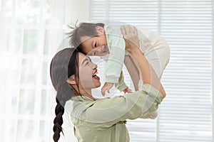 Happy adorable newborn baby playing with mom on bed smiling and cheerful at cozy home. Mom talking with infant baby laughing