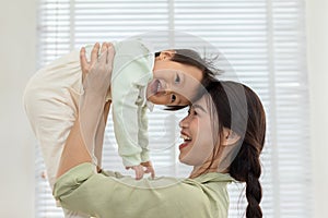 Happy adorable newborn baby playing with mom on bed smiling and cheerful at cozy home. Mom talking with infant baby laughing