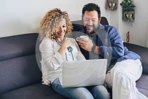 Happy adult aged couple caucasian people at home with personal laptop computer and internet connection - together in indoor