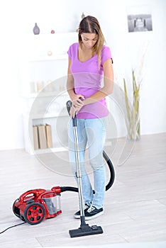 Happy adult blonde girl hoovering in living room and smiling