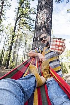 Happy adult caucasian couple enjoy the nature outdoor leisure camping activity - woman legs pov on hammock and man standing with