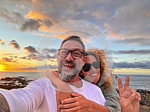 Happy adult couple in love taking selfie picture with romantic wonderful sunset on the ocean in background. Young mature people