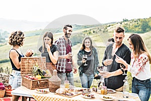 Happy adult friends eating at picnic lunch in italian vineyard outdoor - Young people having fun on gastronomic weekend tuscany