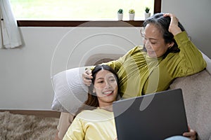 Happy adult granddaughter and senior grandmother having fun enjoying talk sit on sofa in modern living room, smiling old