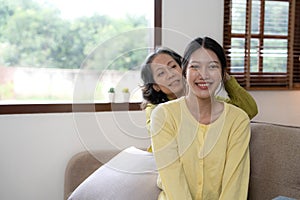 Happy adult granddaughter and senior grandmother having fun enjoying talk sit on sofa in modern living room, smiling old