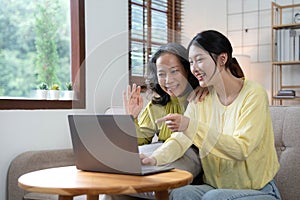 Happy adult granddaughter and senior grandmother having fun enjoying talk sit on sofa in modern living room, smiling old