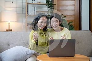 Happy adult granddaughter and senior grandmother having fun enjoying talk sit on sofa in modern living room, smiling old