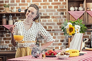 happy adult housewife holding jug of orange juice and looking at camera