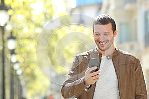 Happy adult man using a smart phone in the street