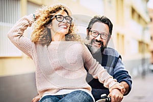 Happy adult mature beautiful couple enjoy and have fun riding a bike together - man carrying woman and laughing a lot - happy