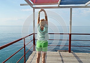 Happy adult woman doing gymnastics on the beach, back view, healthy lifestyle concept