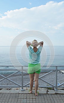 Happy adult woman doing gymnastics on the beach, back view, healthy lifestyle concept
