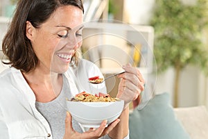 Happy adult woman eating cereal bowl having breakfast at home