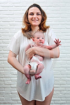 A happy adult woman holds a newborn baby boy against the background of a white brick wall