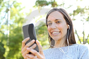 Happy adult woman listening to music looking at you