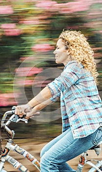 Happy adult woman ride a bike outdoor with flowers in background. Environment and green transport with bycicle. Cheerful modern