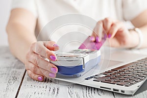 Happy adult woman sitting at home on couch with laptop and credit card. Paying bills and orders. Online shopping and e-commerce co