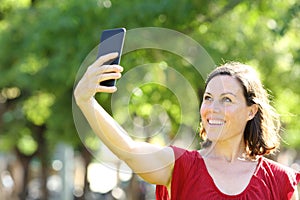 Happy adult woman taking selfie with phone in the park