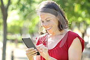 Happy adult woman texting on phone standing in the park