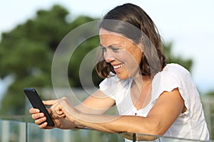 Happy adult woman uses phone on a balcony