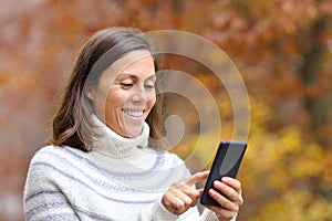 Happy adult woman using smart phone in autumn in a park