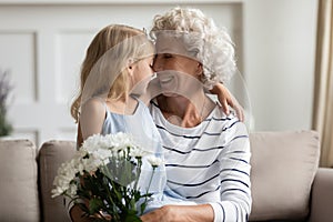 Happy affectionate middle aged grandma touching noses with granddaughter.