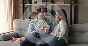 Happy affectionate young family couple drinking coffee resting on sofa.