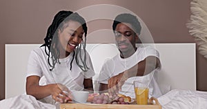 Happy afrcan american woman and man husband and wife sitting in bed awaking eating having breakfast in bed befor hard