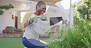 Happy african amercian woman gardening, watering plants in garden